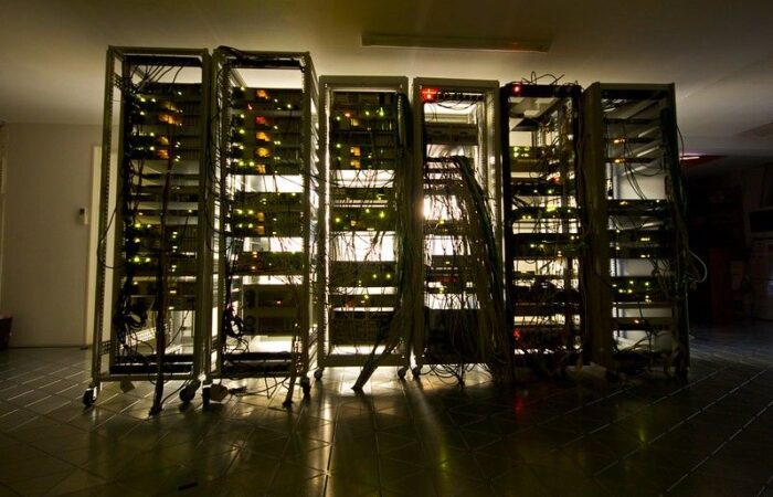 dark room with light coming through the other side of a row of tangled computer servers