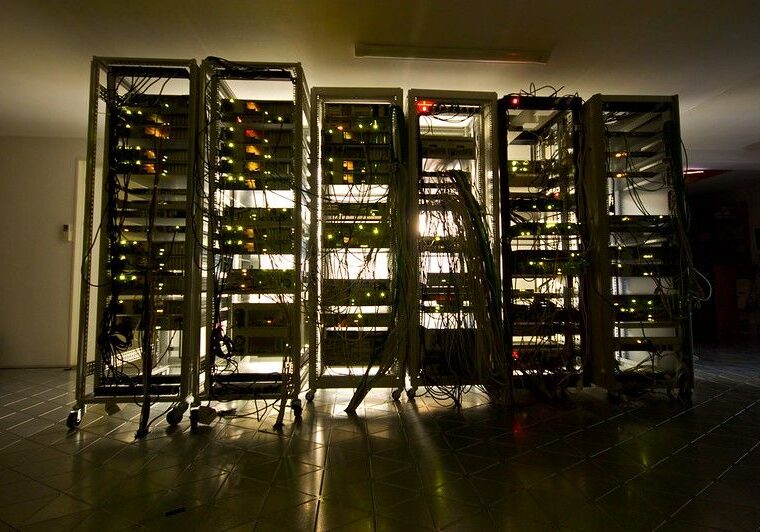dark room with light coming through the other side of a row of tangled computer servers