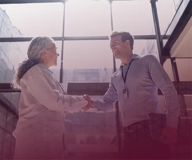 A woman and man shake hands in a corporate office.