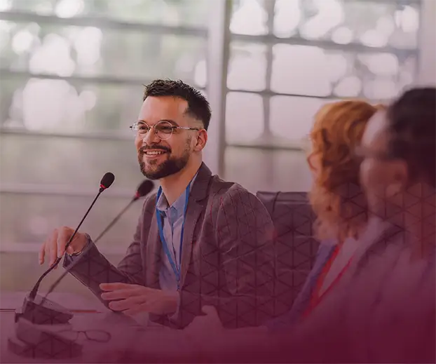 Man speaking into a microphone on a stage on the auad9 Foundation Council page.